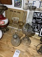 Both glass oil lamps side by side on wooden surface