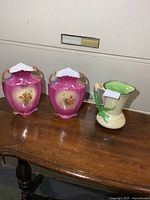 Overall view showing two pink vases and one cream pitcher on wooden table