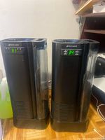 Front view of both Bionaire tower humidifiers powered on showing humidity levels