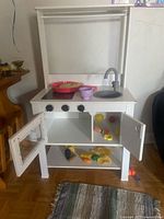 Overall view of white wooden play kitchen with accessories and plastic food pieces