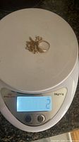 Ring and broken chain on digital scale displaying 2 g