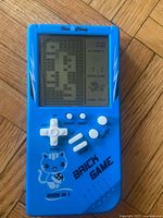 Front view of blue Han Cheng handheld LCD Brick Game showing screen, controls, and printed graphics