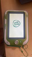 Front view of LeapFrog LeapPad Ultra XDi tablet powering on with LeapFrog logo visible, stylus shown attached