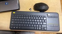 Keyboard with touchpad, mouse and one USB receiver visible on desk, second receiver docked in keyboard