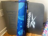 Front view of all three mats standing upright: Everlast grey, blue patterned unbranded, black Reebok