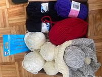 Box containing assorted yarn skeins and packaged knitting tools