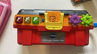 Front of closed VTech Drill & Learn Toolbox Pro showing light-up buttons, speaker grille and coloured gears