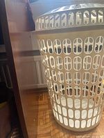 Side view of white plastic round hamper next to furniture