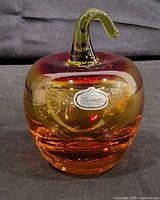 Front view of amber-ruby glass apple with green stem and Rainbow label visible