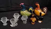 Group shot of all items: four glass egg cups, two large ceramic roosters, three small ceramic ducks