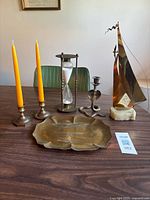 Group view of all items: brass tray, candlesticks with candles, hourglass, snake candlestick, DeMott sailboat sculpture