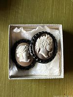 Both cameo brooches in box showing relative sizes and settings