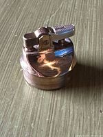 Front view of brass-tone tabletop lighter showing lift-arm mechanism