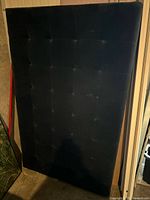 Front view of black/charcoal tufted fabric headboard leaning upright
