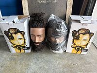 Two boxes, one unbagged mannequin head with topknot and beard, one plastic-wrapped mannequin head