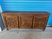 Front view of credenza showing three carved doors and overall form