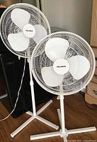 Two Pelonis pedestal fans standing side by side showing full height and bases