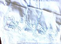 Section of tablecloth showing blue embroidered floral motifs and scalloped edge