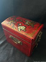 Closed red lacquer box showing floral motif and brass hardware