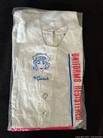 Uniform in original plastic bag showing embroidery and buttons