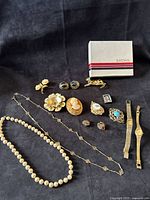 Full layout of watches, necklaces, brooches, earrings, and Eaton’s box on dark background