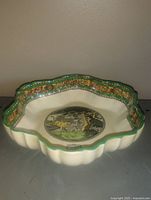 Side view of scalloped ceramic dish showing cream glaze, green rim, central bull scene