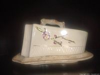 Left side view of ceramic butter dish showing floral relief and branch handle