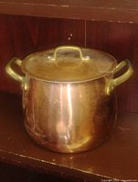 Front view of copper stock pot with brass handles and lid