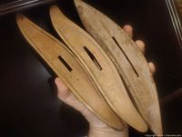 three wooden weaving shuttles held in hand showing exterior slots