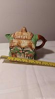 Front view of porcelain cottage teapot with tape measure for scale