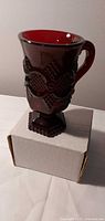 Side view of ruby red pressed glass handled pedestal mug on box