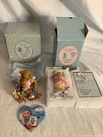 Lot overview showing both boxed figurines, one unboxed figurine, styrofoam-encased figurine, event pin