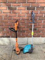 Both trimmers standing upright against brick wall