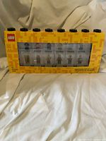 Front view of sealed yellow Lego minifigure display case showing clear compartments and black top studs