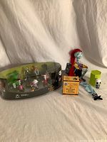 Full lot overview showing boxed figurine set, Sally doll, cross-stitch kit, mystery figure, green holder