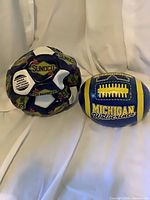 Sunoco soccer ball and Michigan Wolverines football side by side, both deflated
