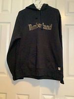 Front view of black Timberland hoodie hanging, showing overall garment