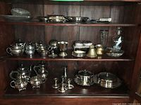 Wide view of three shelves of silver-plated items in cabinet