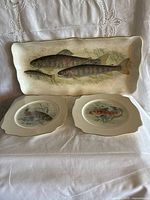Front view of platter and both plates showing fish designs and gilt rims