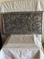 Full view of rectangular silver-tone embossed wall plaque on chair