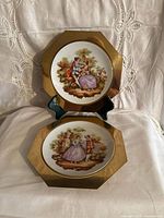 Two octagonal brass wall plates showing front porcelain scenes