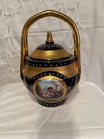 Front view of cobalt blue porcelain covered jar with gold gilt, handle and painted scene