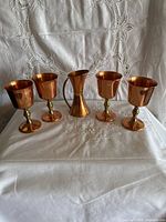 Four copper goblets and copper jug front view