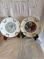 Front view of both plates on stands showing embossed holly rims and central scenes