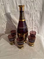 Front view of amethyst decanter with six glasses showing gold and white banding