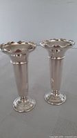 Both matching silver-plated bud vases standing side by side