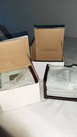 Two opened white boxes showing packaged coaster sets and stands
