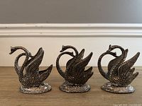 Front view of three metal swan napkin holders
