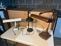 Three lamps on table: brown articulating lamp, black and glass lamp, white desk lamp