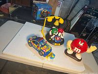 Overview of all three M&M items on table: telephone, police car dispenser, red character dispenser